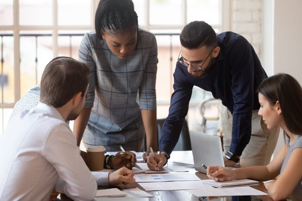 Five employees examining papers on a conference table as they discuss the benefits of document digitizing services 